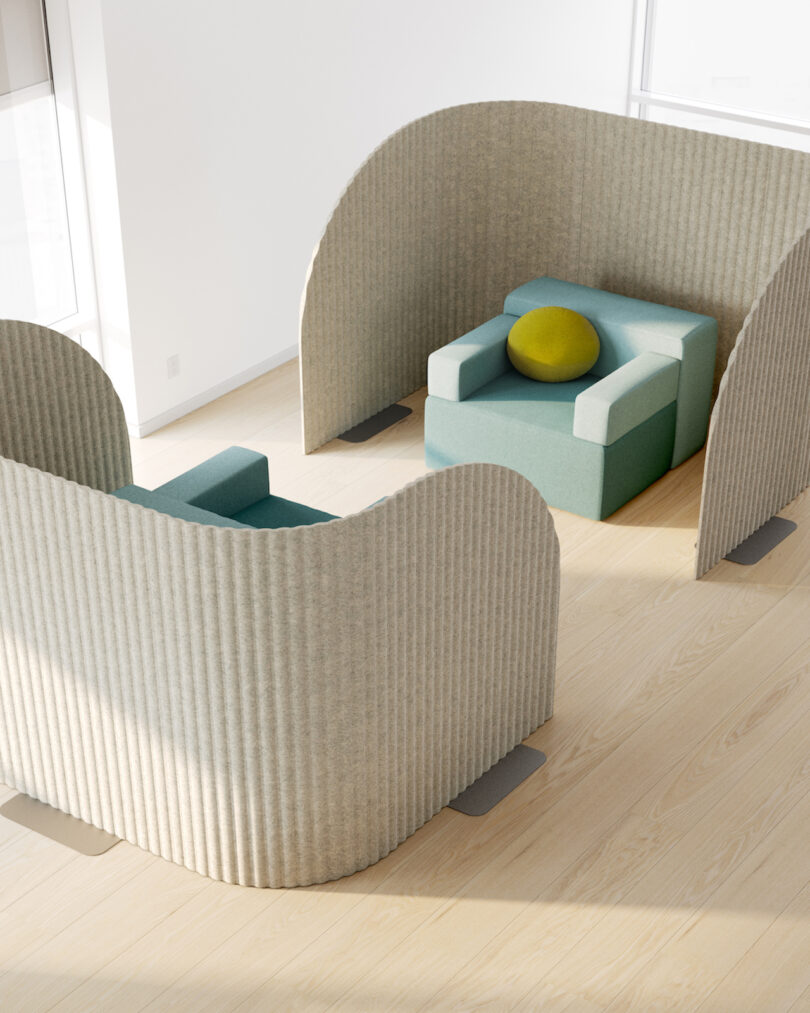 Two teal armchairs with a yellow cushion are positioned within light gray curved privacy screens on a wooden floor