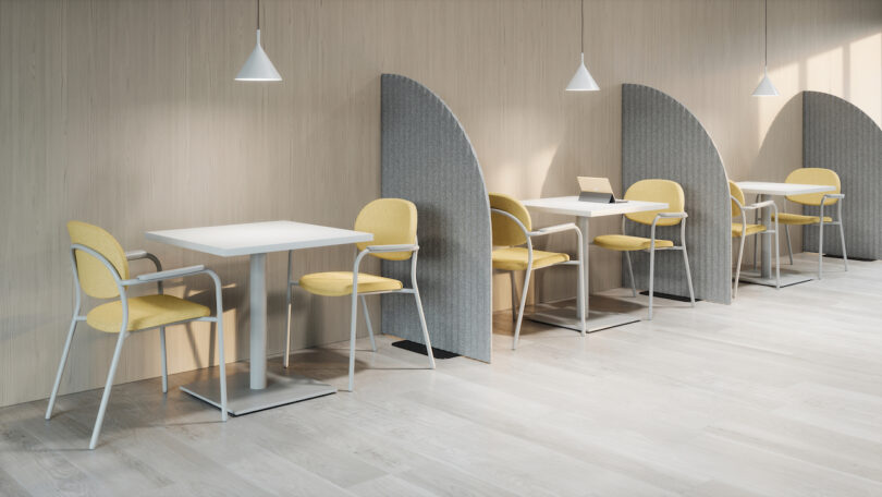 A row of tables with yellow chairs and gray dividers in a modern, well-lit workspace