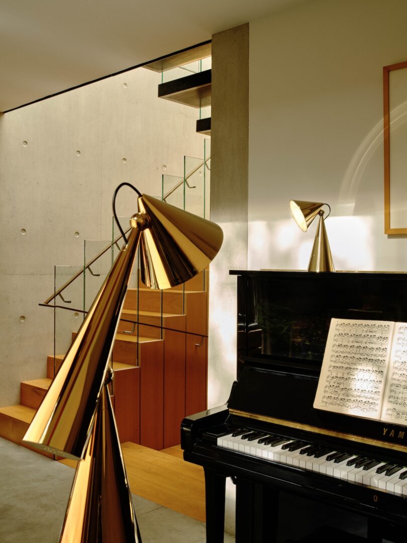 A modern interior with a black piano and music sheet, gold lamps, wooden staircase, and concrete wall