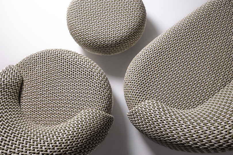 Overhead image of a modern woven furniture set consisting of a couch, an armchair, and a round ottoman set against a plain white background.