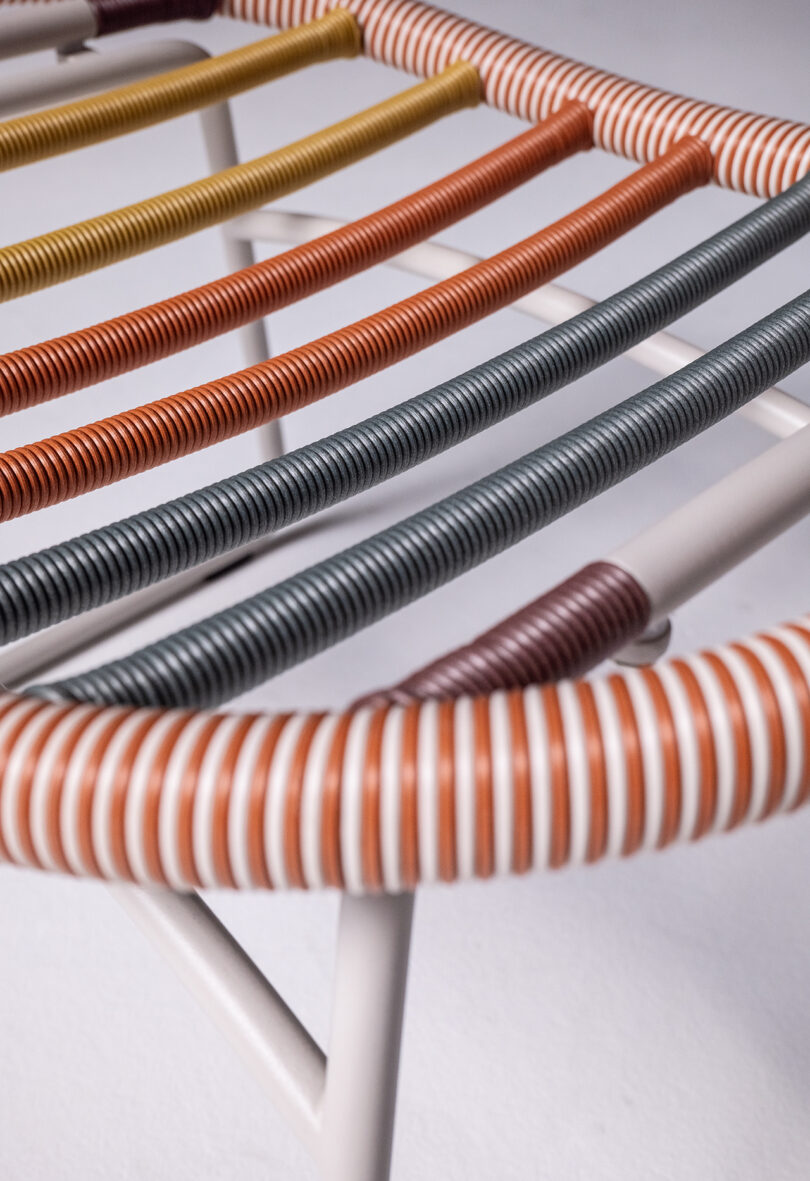 Close-up of a minimalist chair with a white metal frame and multicolored woven seat in shades of yellow, orange, red, blue, and white.