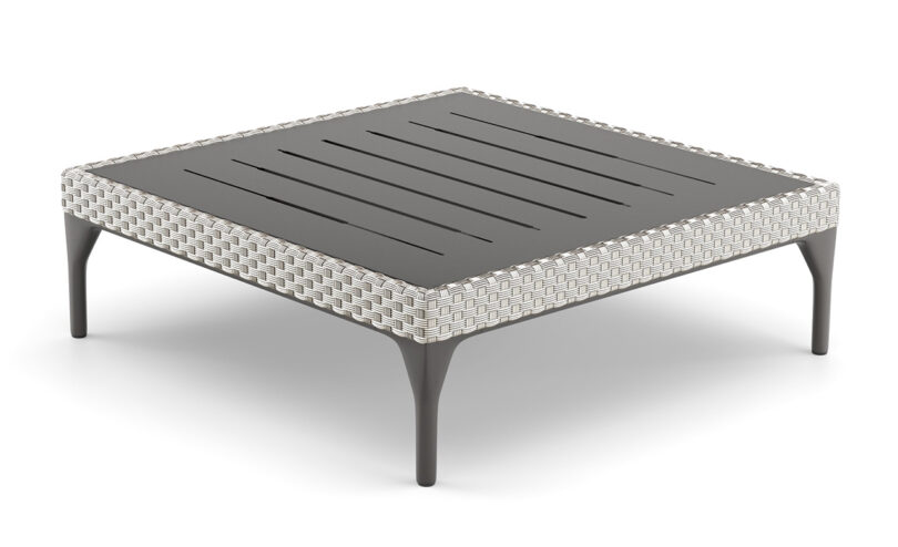 A square, modern footstool with a slatted black top and wicker sides, supported by four black legs.