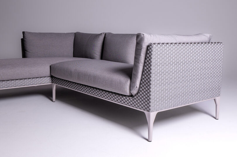 A modern L-shaped gray sectional sofa with a woven backrest and metal legs.