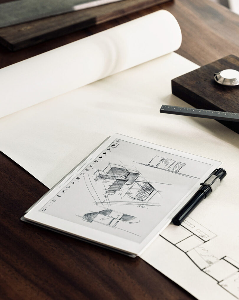 A desk with architectural sketches, a pen, and a ruler on top of a drawing pad.