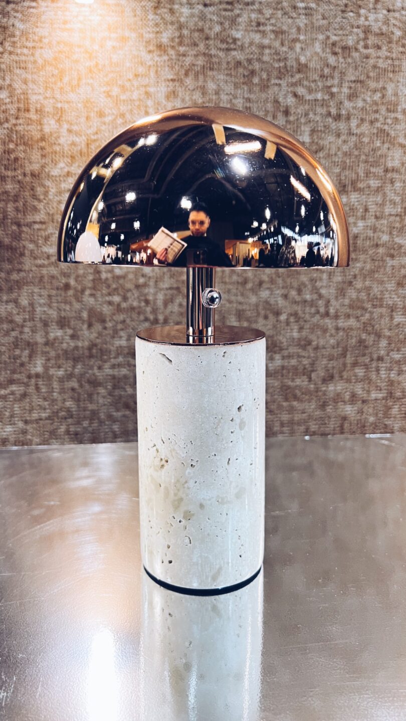 A modern table lamp with a cylindrical stone base and a reflective half-dome metal shade, capturing the serene ambiance of a