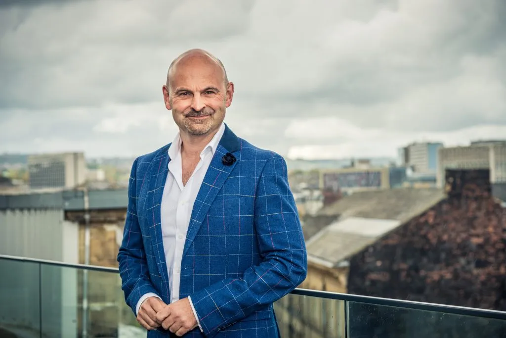 Richard Cristofoli in a blue suit standing on a balcony overlooking a city.