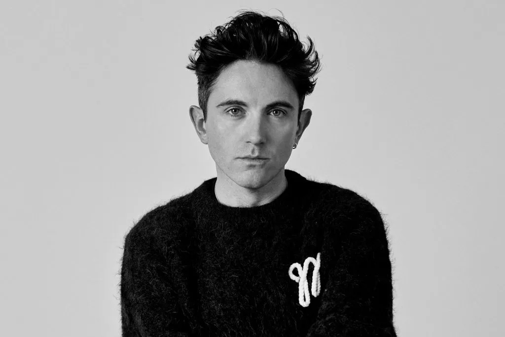 Daniel Fletcher in black jumper with embroidered 'M' logo against plain background
