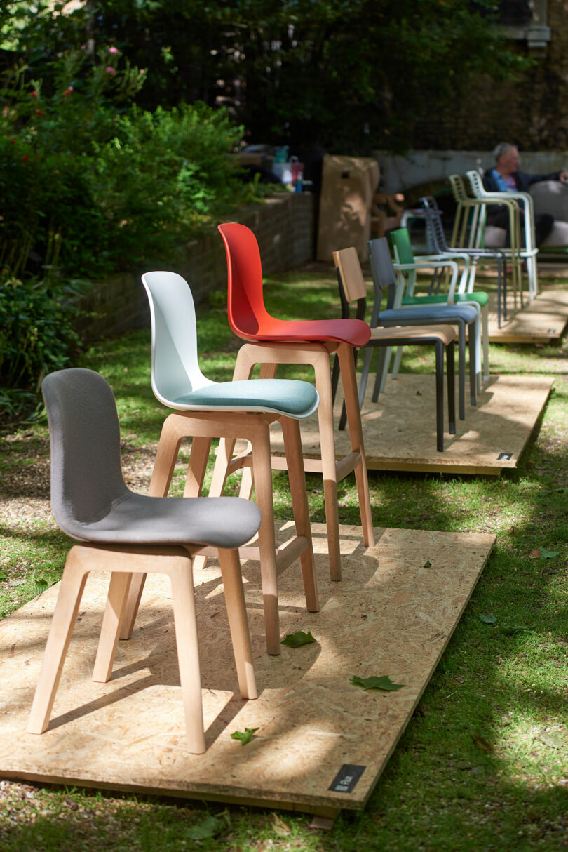 A display of wooden chairs with various colored seats, reminiscent of the CDW 2025 Product Awards, is arranged on a wooden platform outdoors, surrounded by lush greenery.