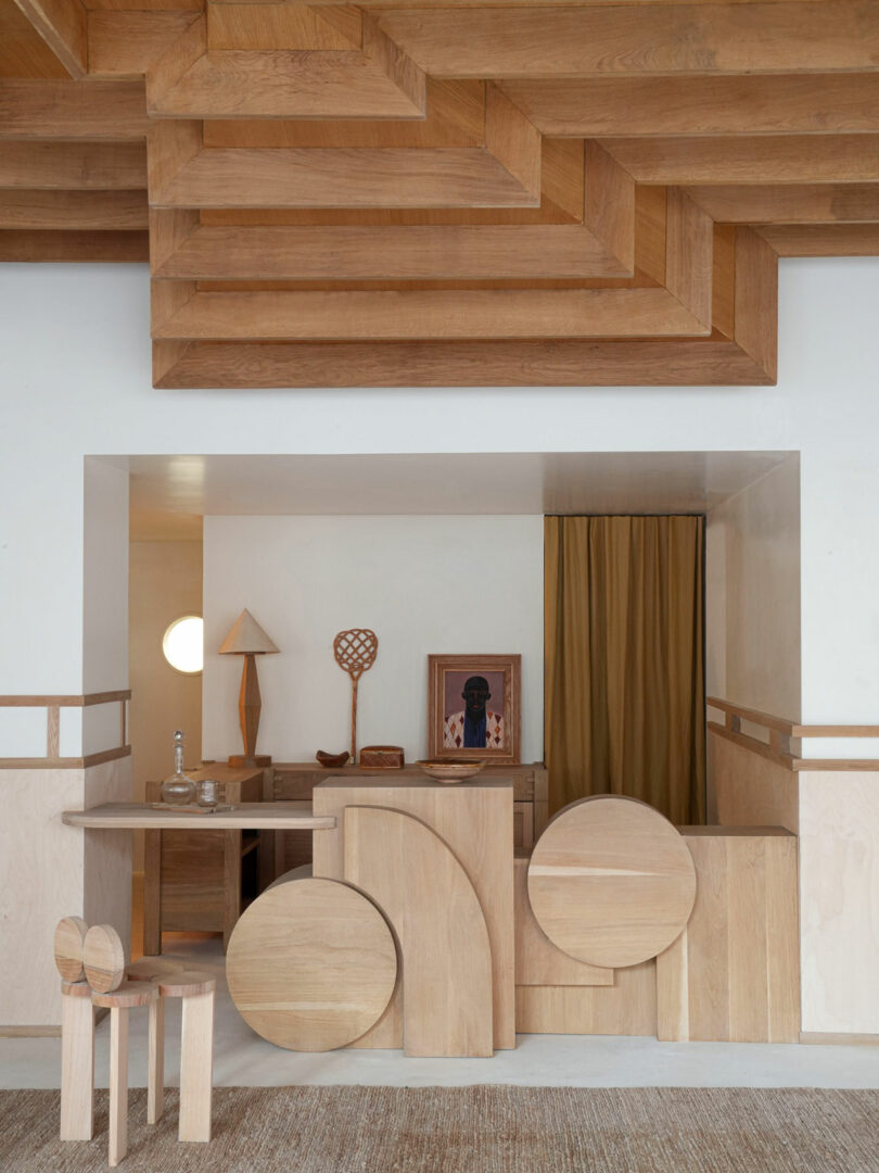 The interior captures a minimalist wooden design theme with geometric shapes, a chair, and artwork. A small lamp casts a warm glow, while the curtain partially obscures the background in this policronica-inspired space.
