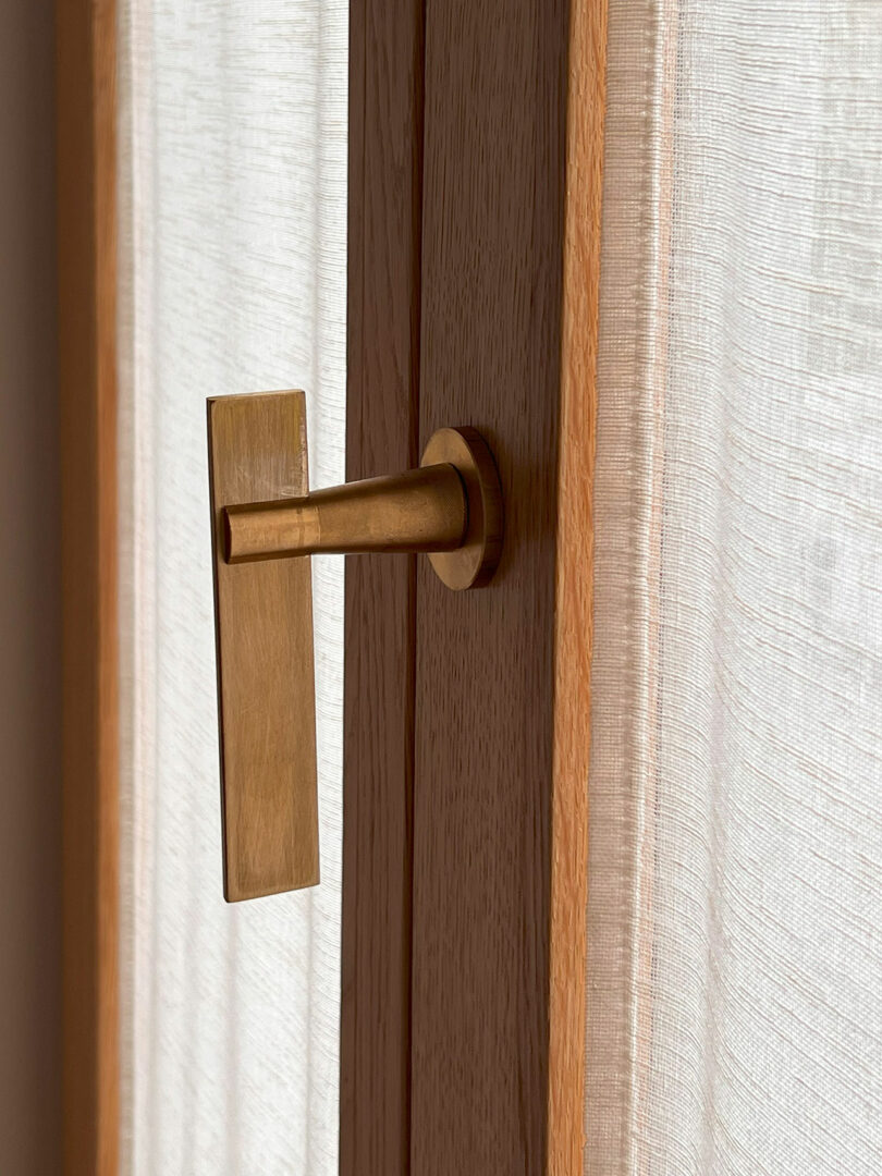 A Policronica wooden door with a brass handle stands elegantly next to a sheer curtain.