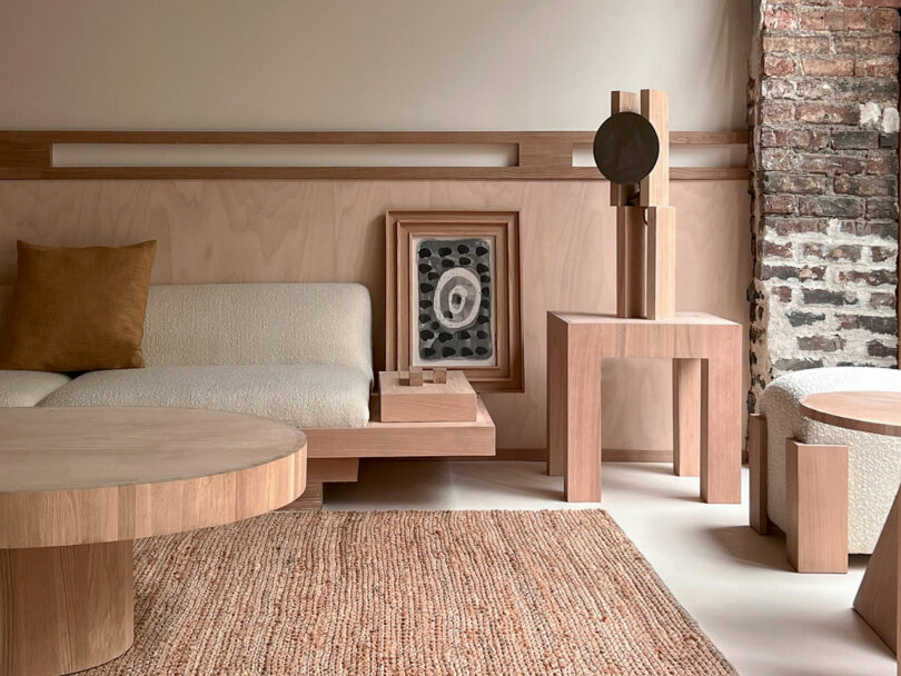 The minimalist living room features wooden furniture, a beige sofa, and abstract artwork. A textured rug complements the exposed brick wall, creating a striking contrast with the modern decor. The Policronica touch infuses harmony into this refined space.