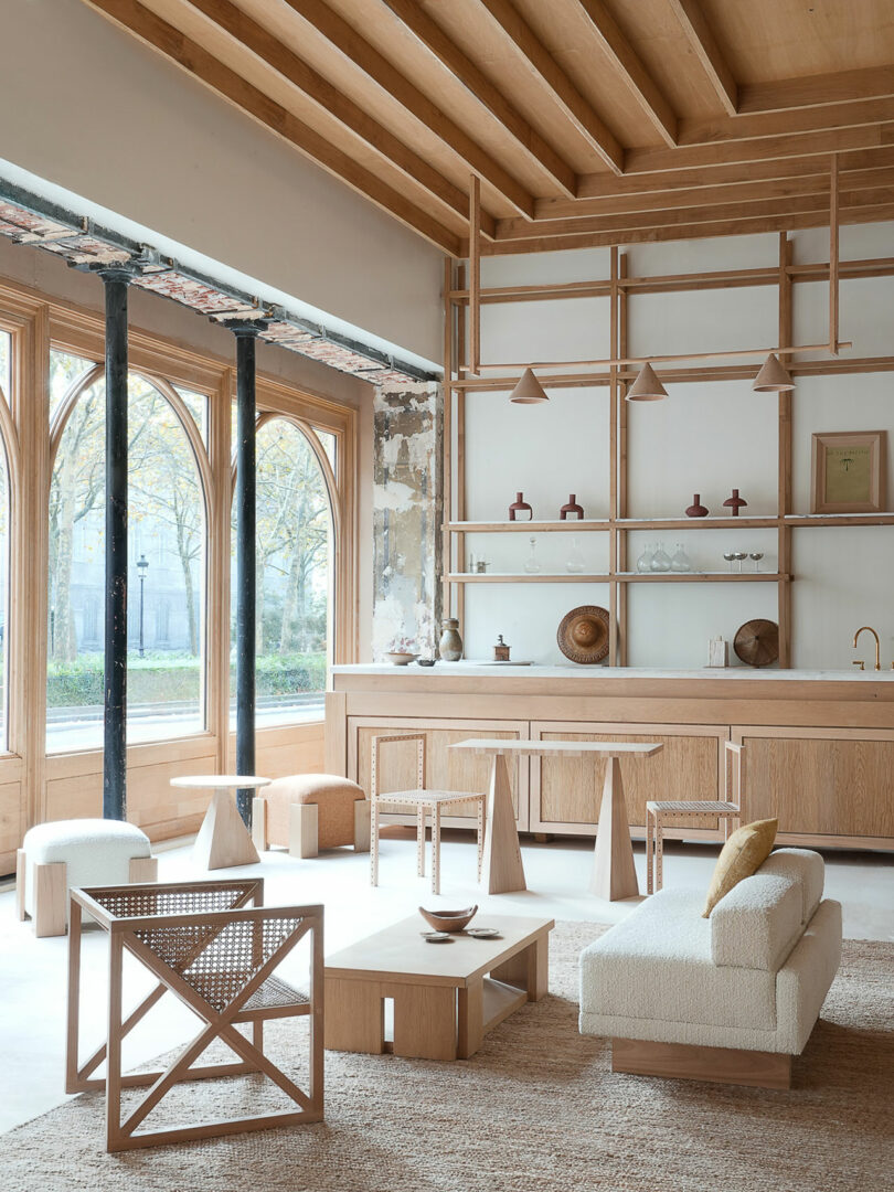 A modern, minimalistic room features wooden furniture and arched windows that highlight its Policronica style. The high ceiling with exposed beams adds character, while shelves display decorative items, perfectly complementing the light, neutral decor.
