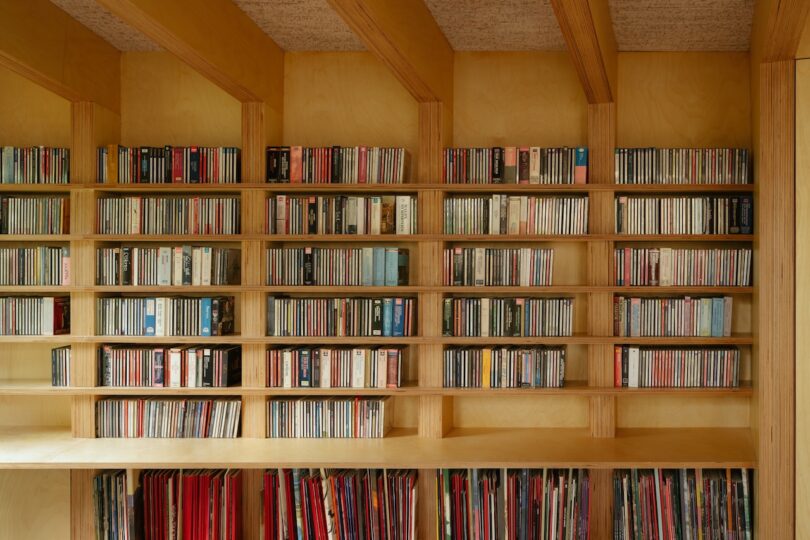 Wooden shelves filled with neatly arranged CDs and vinyl records in a room with a wooden interior.