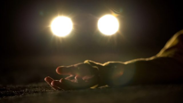 Bloody female victim of deadly car accident lying on road, close-up view at body