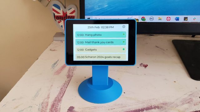 Hands-on-This-35-inch-smart-display-makes-my-digital-calendars-more.jpg A blue DeskBuddy powered on and sitting on top of a desk, next to a computer monitor.