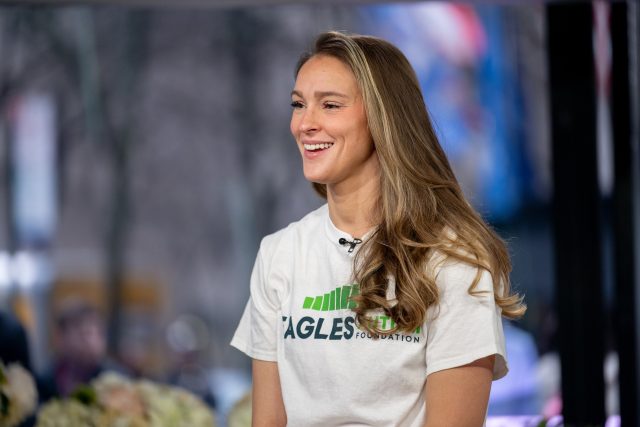 How-Trump-news-and-American-politics-will-be-filtered-through.jpg Kylie Kelce in a white T-shirt and a collar microphone, with long blond hair and a smile.