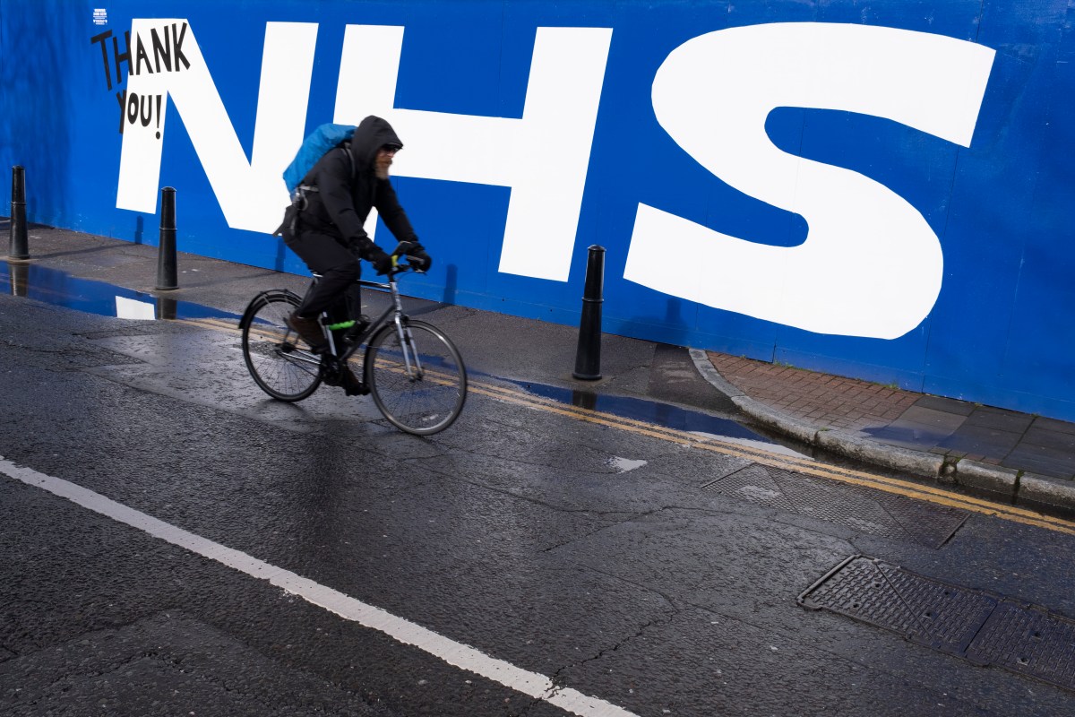 UK-healthcare-giant-HCRG-confirms-hack-after-ransomware-gang-claims.jpg bike rider passes 'NHS' in large white letters on blue wall