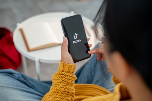 What-it-Means-for-Travel.jpg A close-up of a woman using the TikTok application on her iPhone while sitting on a couch at home.