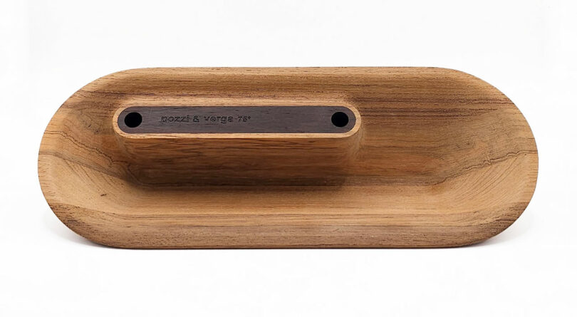Wooden, oval-shaped object with a recessed area, featuring a rectangular, dark wooden inlay with two circular holes.