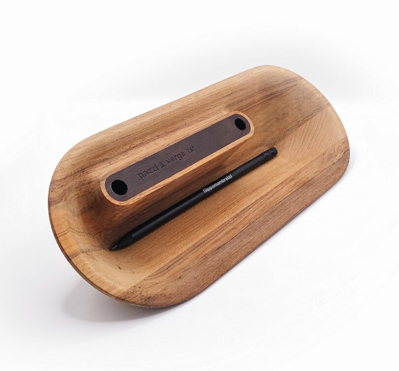 A wooden desk organizer with a black pen placed in a groove, featuring a label with engraved text.