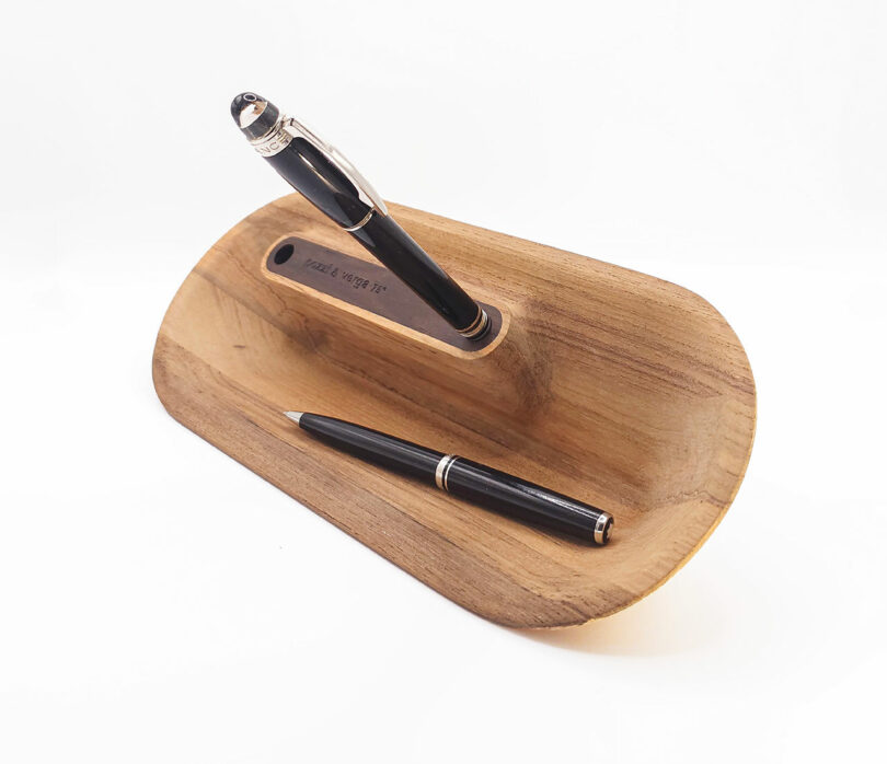Wooden pen holder with two pens, one upright and one lying down, on a white background.