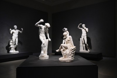 Several ancient sculptures of nude men and women in a darkened room.