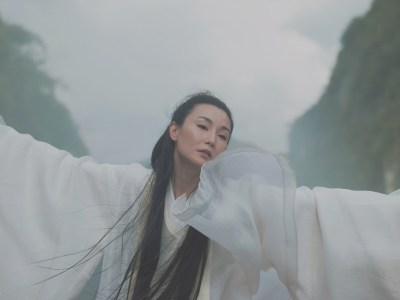 A woman in flowy fabric waving her arms in a mountainous landscape.