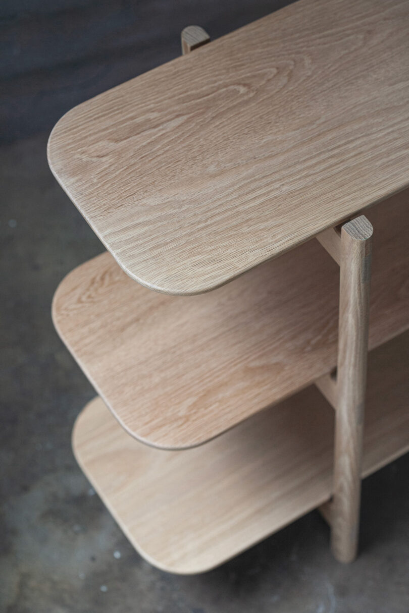 Three-tier wooden shelf with rounded edges, viewed from above, set against a dark background