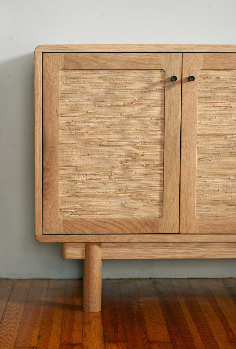 Wooden cabinet with textured panel doors and minimalistic handles, resting on a wooden floor against a light wall