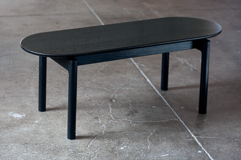 A black oval coffee table with four legs on a concrete floor