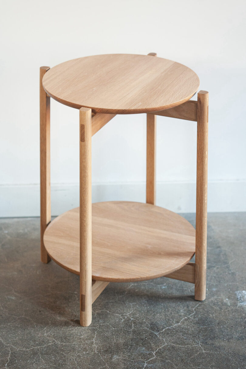 A wooden side table with two circular tiers stands on a concrete floor