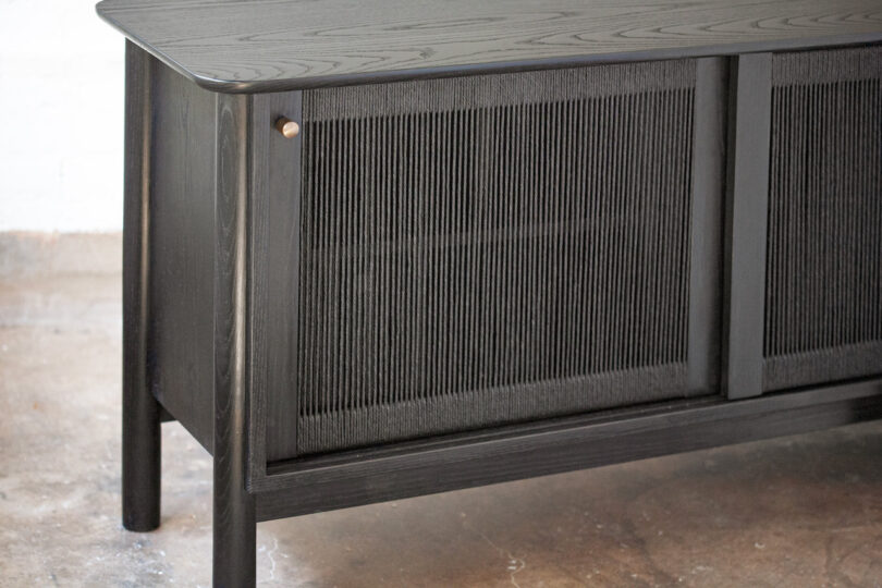 Black wooden sideboard with textured sliding doors on a concrete floor