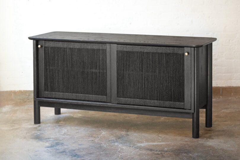A modern black wooden cabinet with two sliding doors stands against a white brick wall on a concrete floor