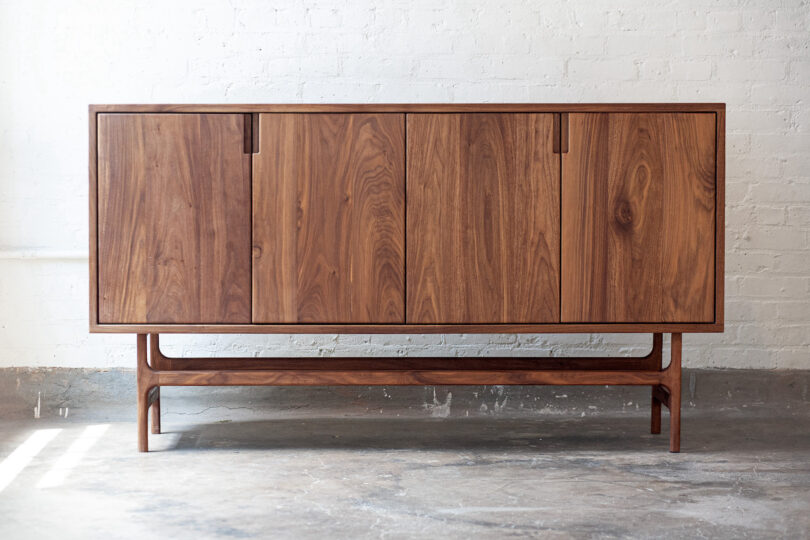 Wooden sideboard with four doors on a concrete floor against a white brick wall