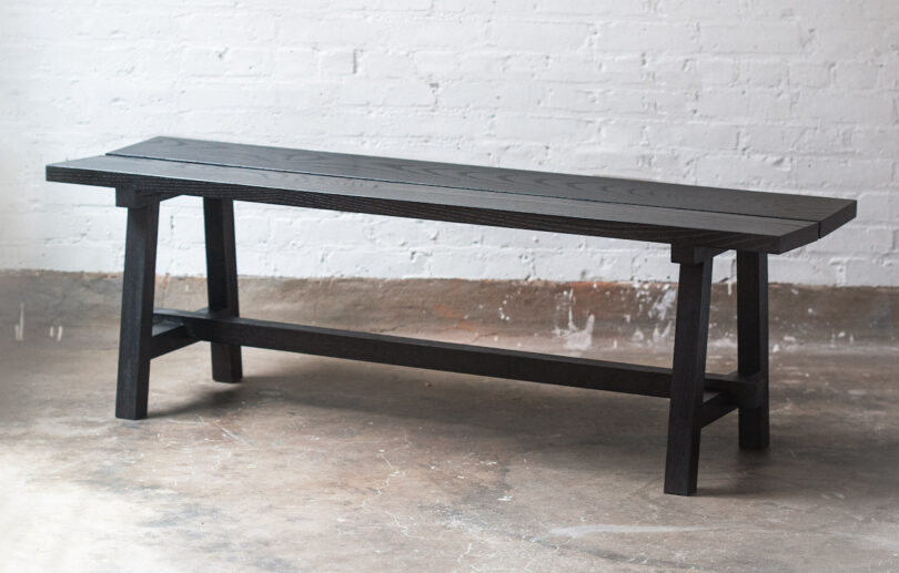 A wooden bench with a dark finish is placed against a white brick wall on a concrete floor