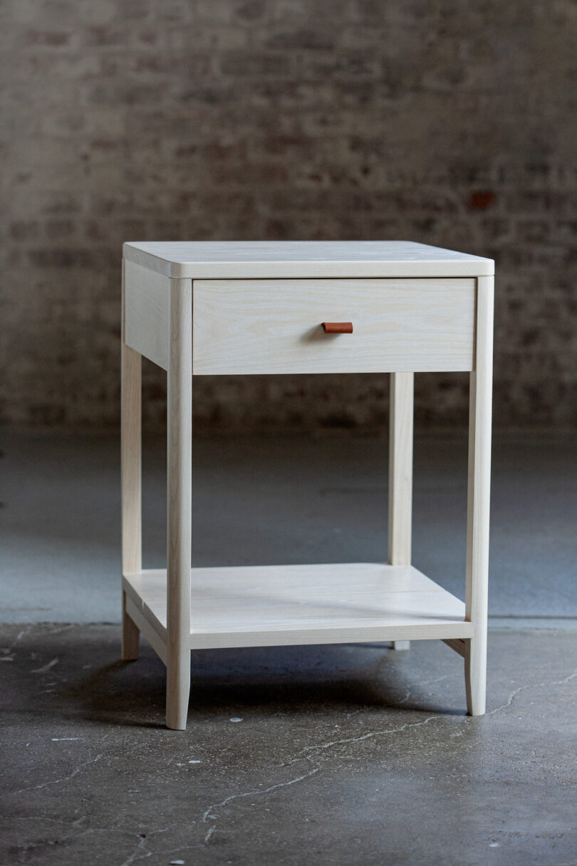 A wooden nightstand with one drawer and a lower shelf, set against a textured wall