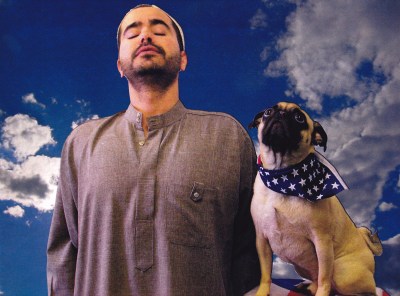 A Brown man standing beside a dog with an American flag bandana.