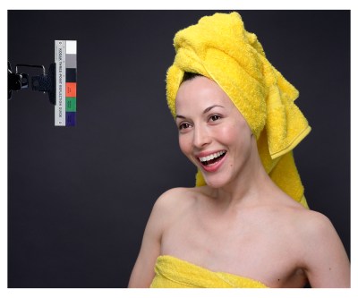 A smiling woman wearing a yellow towel covering her chest and a yellow towel as a turban. Beside her is a color bar.