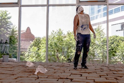 A man with a fabric across his face standing on top of a floor composed of adobe bricks.