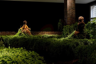 Kudzu covering a gallery that has in it two sculptures of humanoid figures.