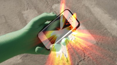 A hand in a green glove holding an iPhone that emits golden light.