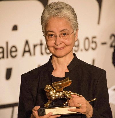 A smiling woman holding a statue of a winged golden lion.