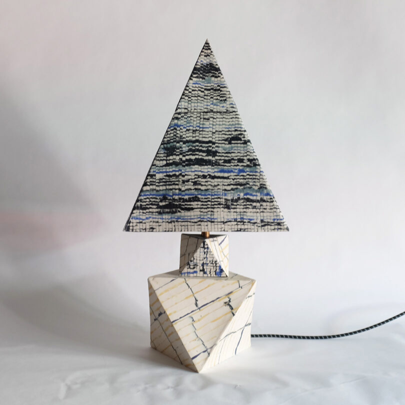 A triangular patterned lamp shade on a geometric, marble-like base with a zigzag pattern. A cord extends from the base.