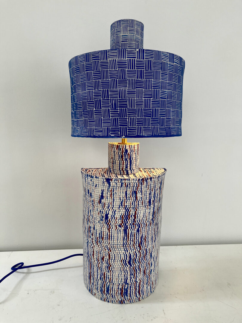 Table lamp with a blue patterned shade and a textured multicolored base on a white background.