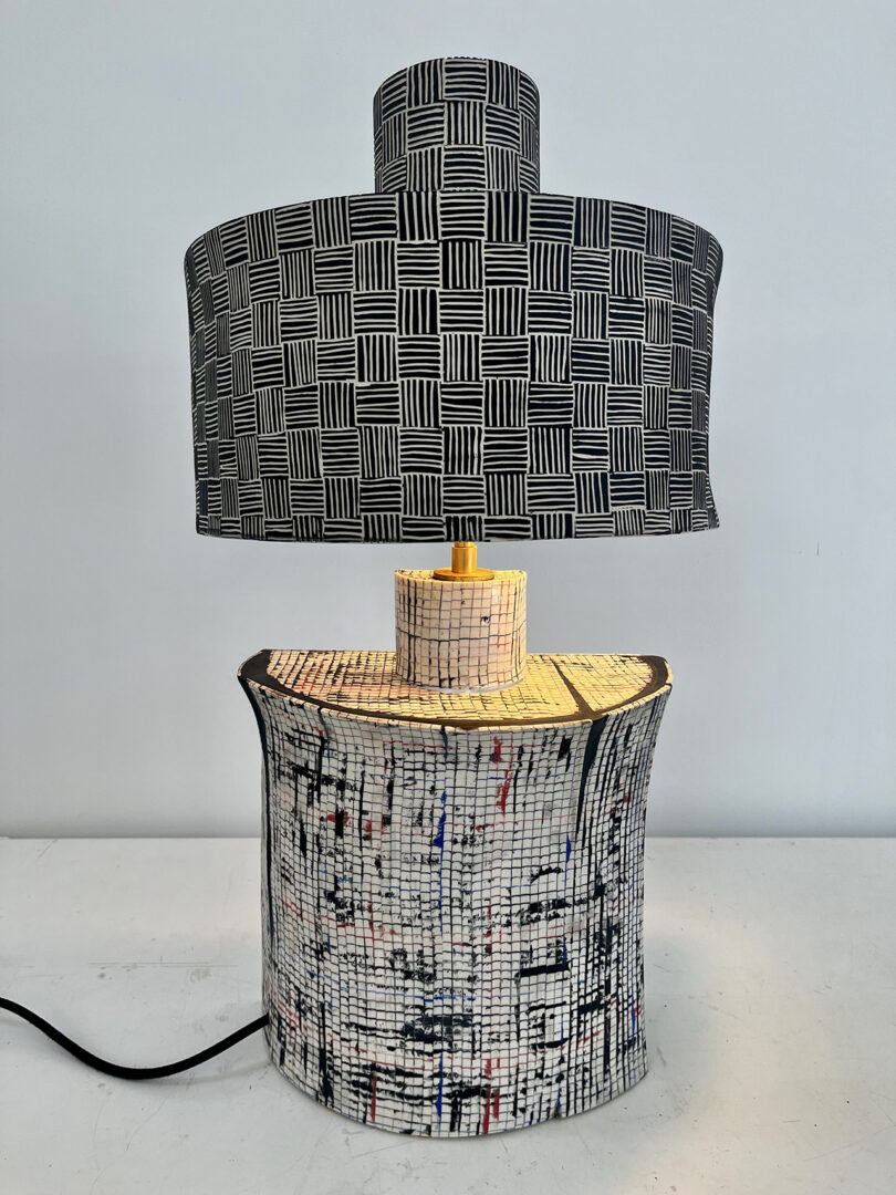 A table lamp with a grid-patterned black and white shade and a textured, multicolored base.