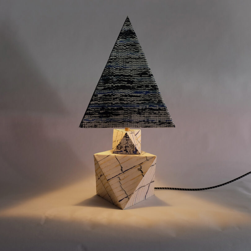 A modern table lamp with a triangular, marbled shade and a geometric, marbled base, set on a plain background.