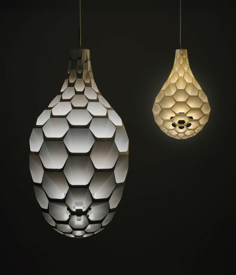 Two teardrop-shaped pendant lights with hexagonal patterns, one larger and white, the other smaller and yellow, suspended against a dark background.