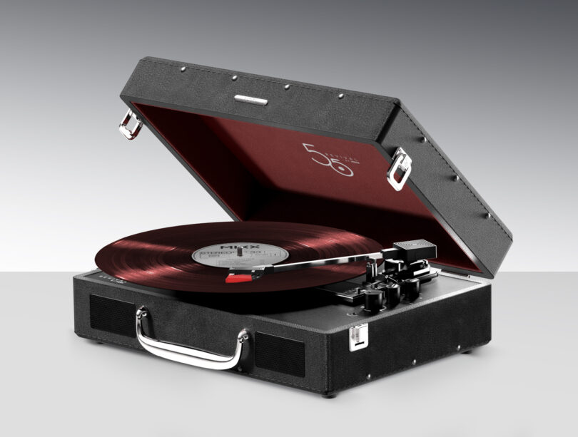 A black portable record player with a red interior, featuring a spinning vinyl record and control knobs on the front.