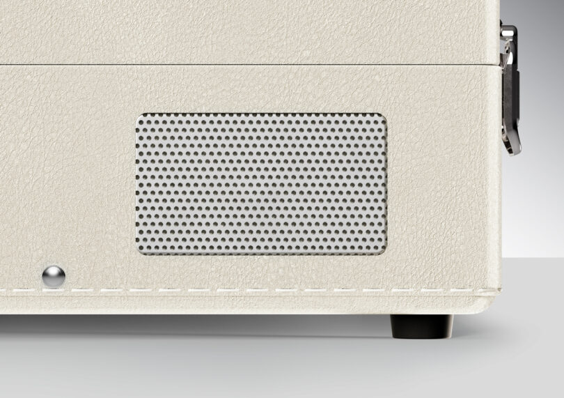 Close-up of a white textured speaker with visible perforated grille and a small round silver button on a gray background.