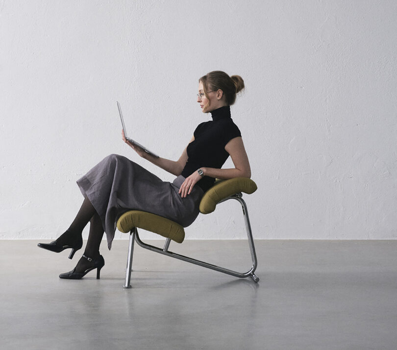 A modern chair with mustard-yellow cushions and a sleek metal frame, featuring a distinctive angled design, positioned on a light grey floor.